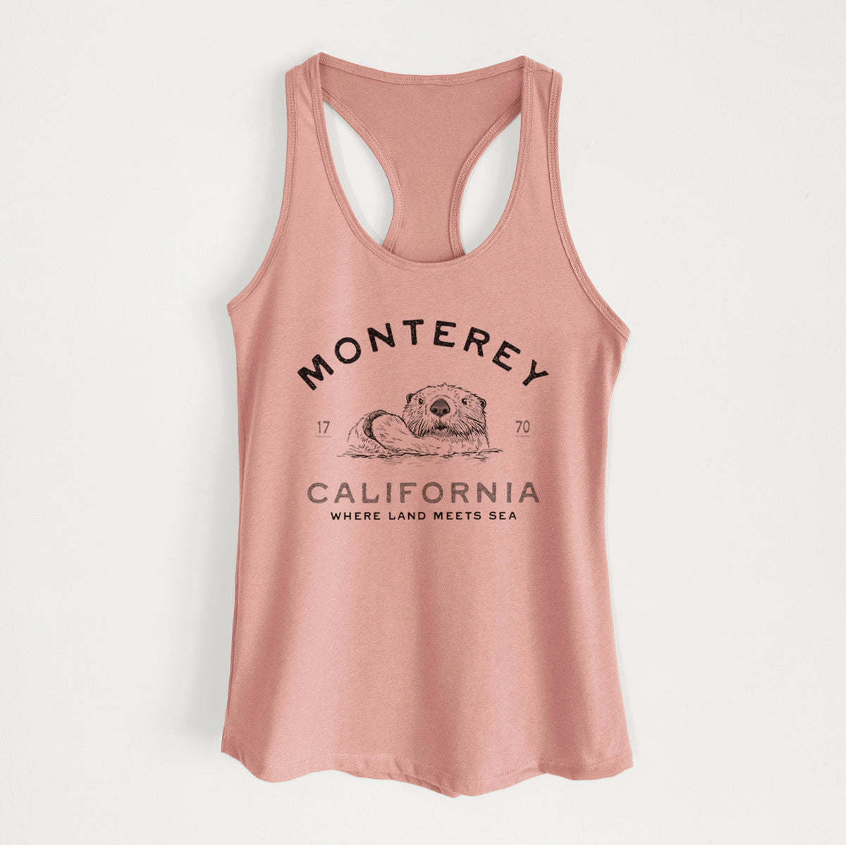 Desert pink women's racerback tank top laid flat, printed with a black ink sea otter floating on its back, with the words Monterey California, 1770, Where Land Meets Sea.