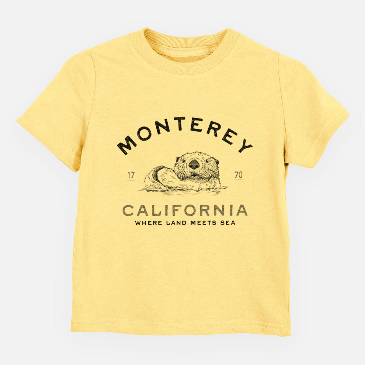 Butter yellow toddler t-shirt laid flat, printed with a black ink sea otter floating on its back, with the words Monterey California, 1770, Where Land Meets Sea.