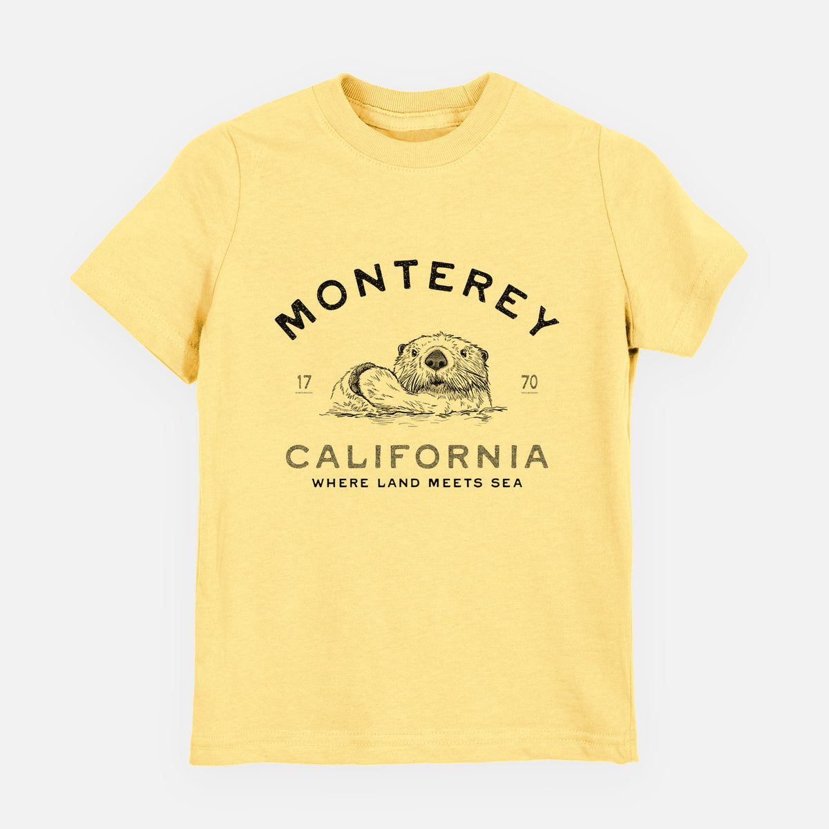 Butter yellow youth t-shirt laid flat, printed with a black ink sea otter floating on its back, with the words Monterey California, 1770, Where Land Meets Sea.