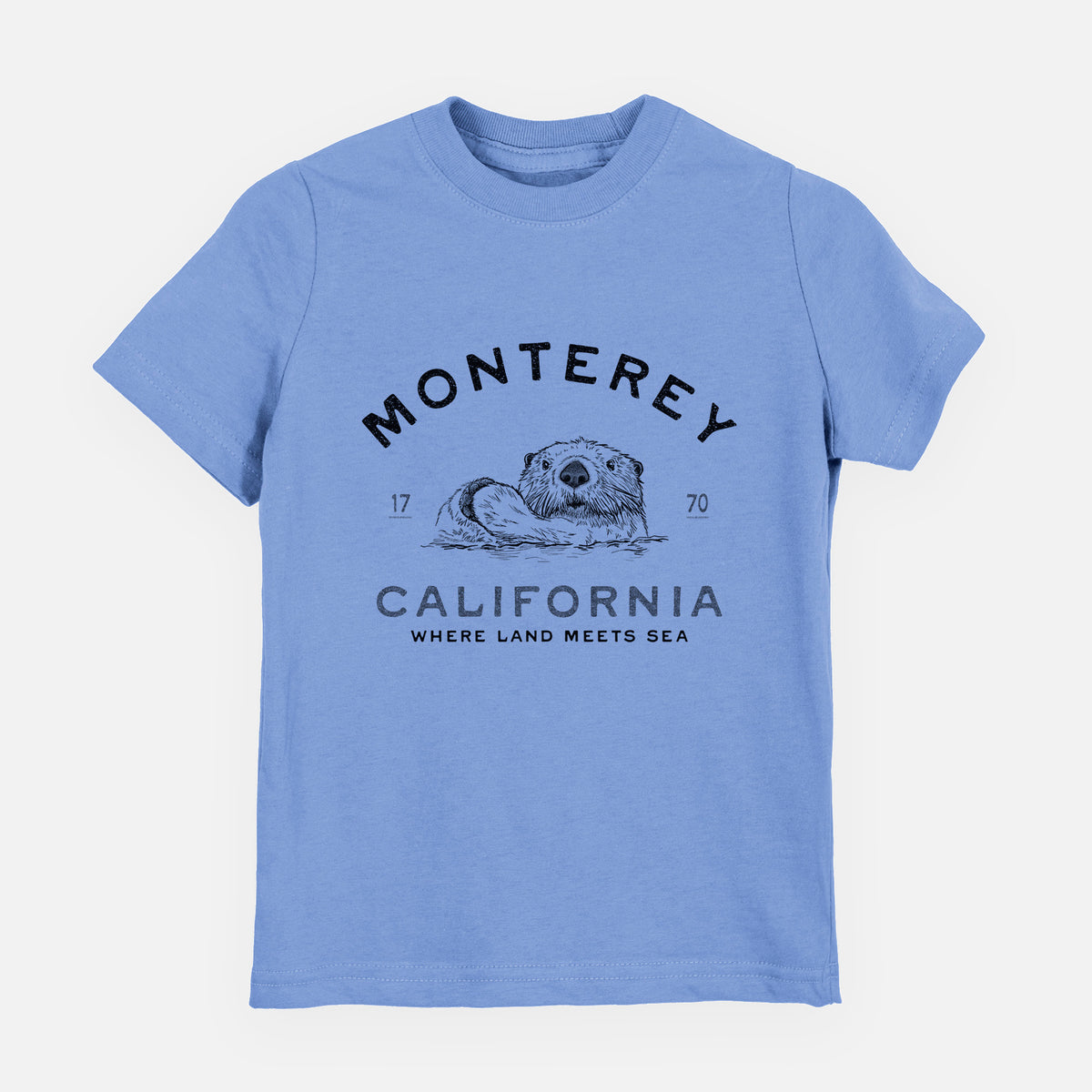 Carolina blue youth t-shirt laid flat, printed with a black ink sea otter floating on its back, with the words Monterey California, 1770, Where Land Meets Sea.