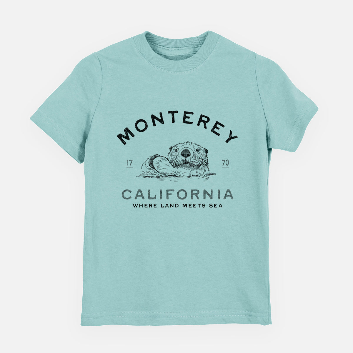 Saltwater youth t-shirt laid flat, printed with a black ink sea otter floating on its back, with the words Monterey California, 1770, Where Land Meets Sea.