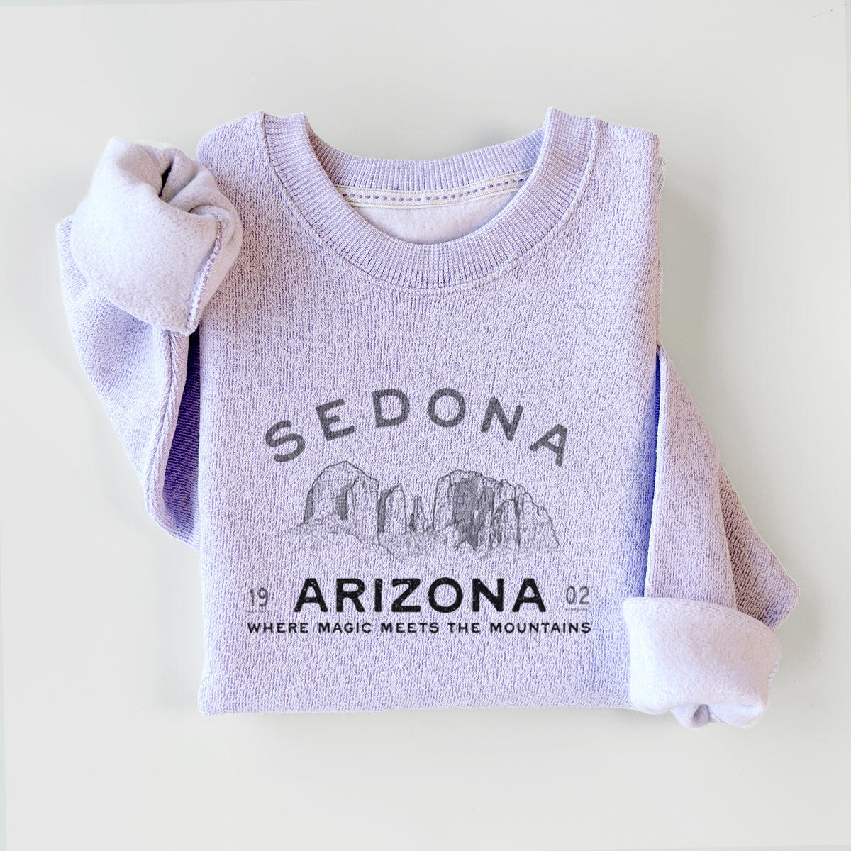 Ice purple knit sweatshirt printed with black ink red rock buttes with the words Sedona Arizona, Where Magic Meets the Mountains, styled flat.