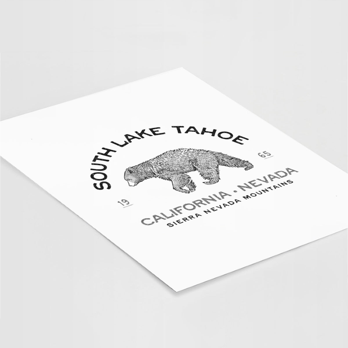 Art print of a black ink bear with the words South Lake Tahoe, California - Nevada, Sierra Nevada Mountains, lying at an angle on a white surface.