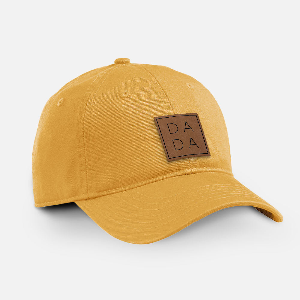 Beehive yellow cotton baseball hat with a brown leather patch engraved with the word DADA stacked in a square on the front.