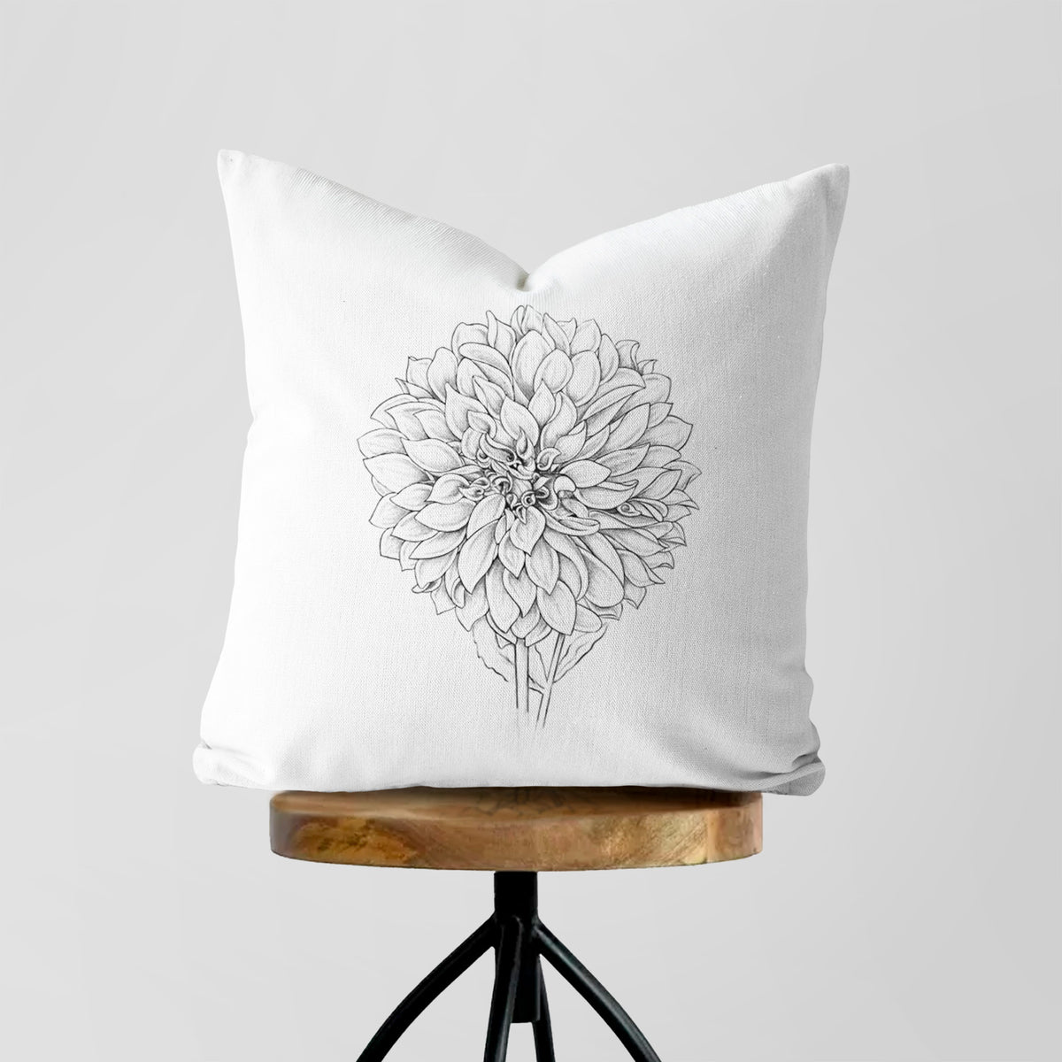 White pillow cover printed with a detailed black ink line drawing of a Cafe au Lait dahlia bloom, on a wooden stool.