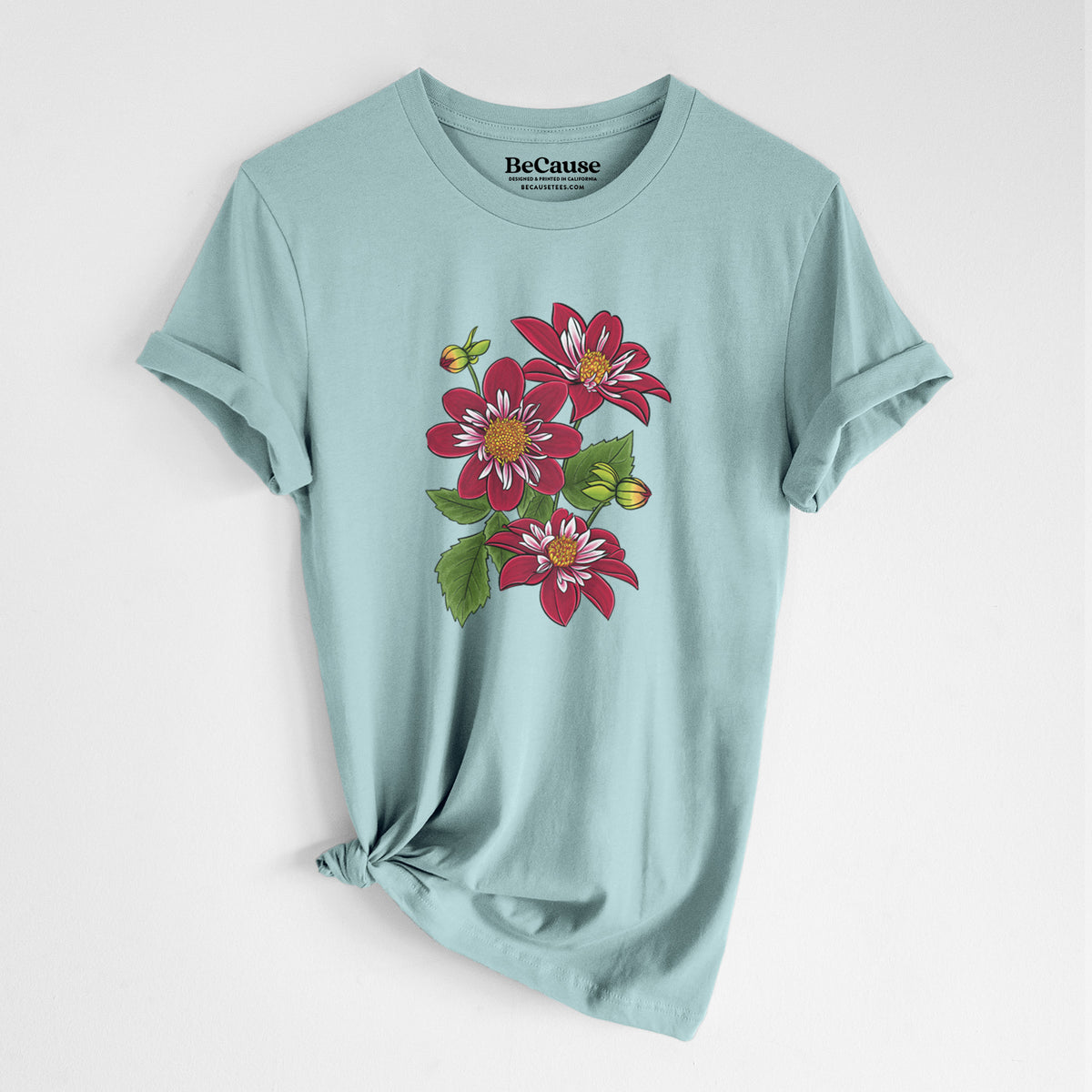 Dusty blue lightweight cotton t-shirt laid flat with the sleeves rolled, printed with a full-color illustration of deep red dahlia flowers with green leaves and a small bee.