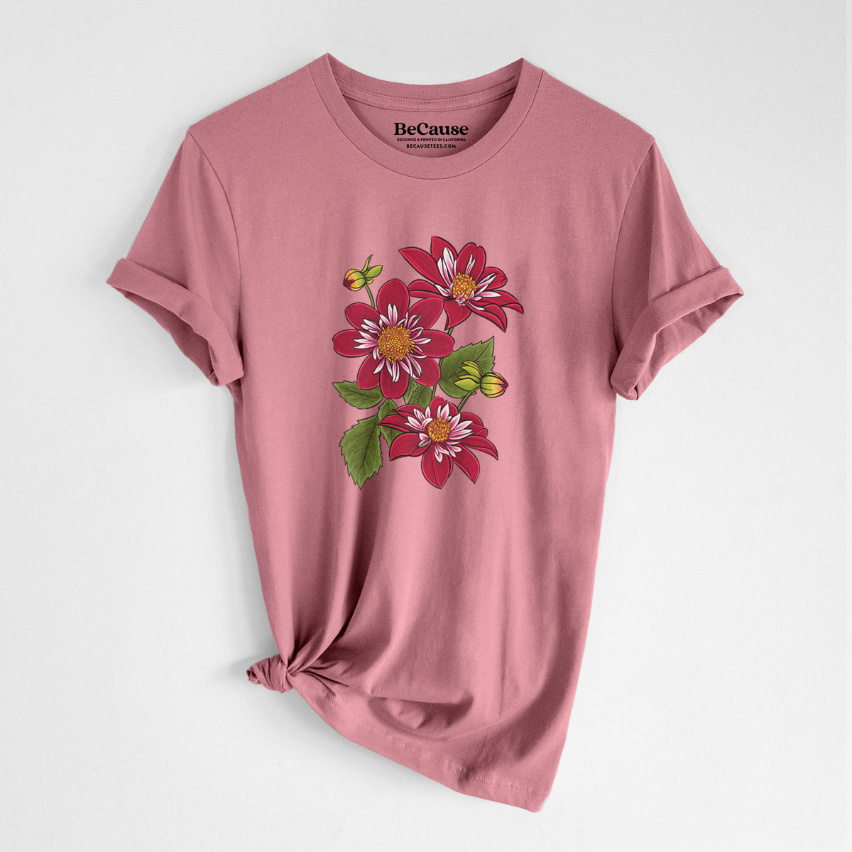 Mauve pink lightweight cotton t-shirt laid flat with the sleeves rolled, printed with a full-color illustration of deep red dahlia flowers with green leaves and a small bee.