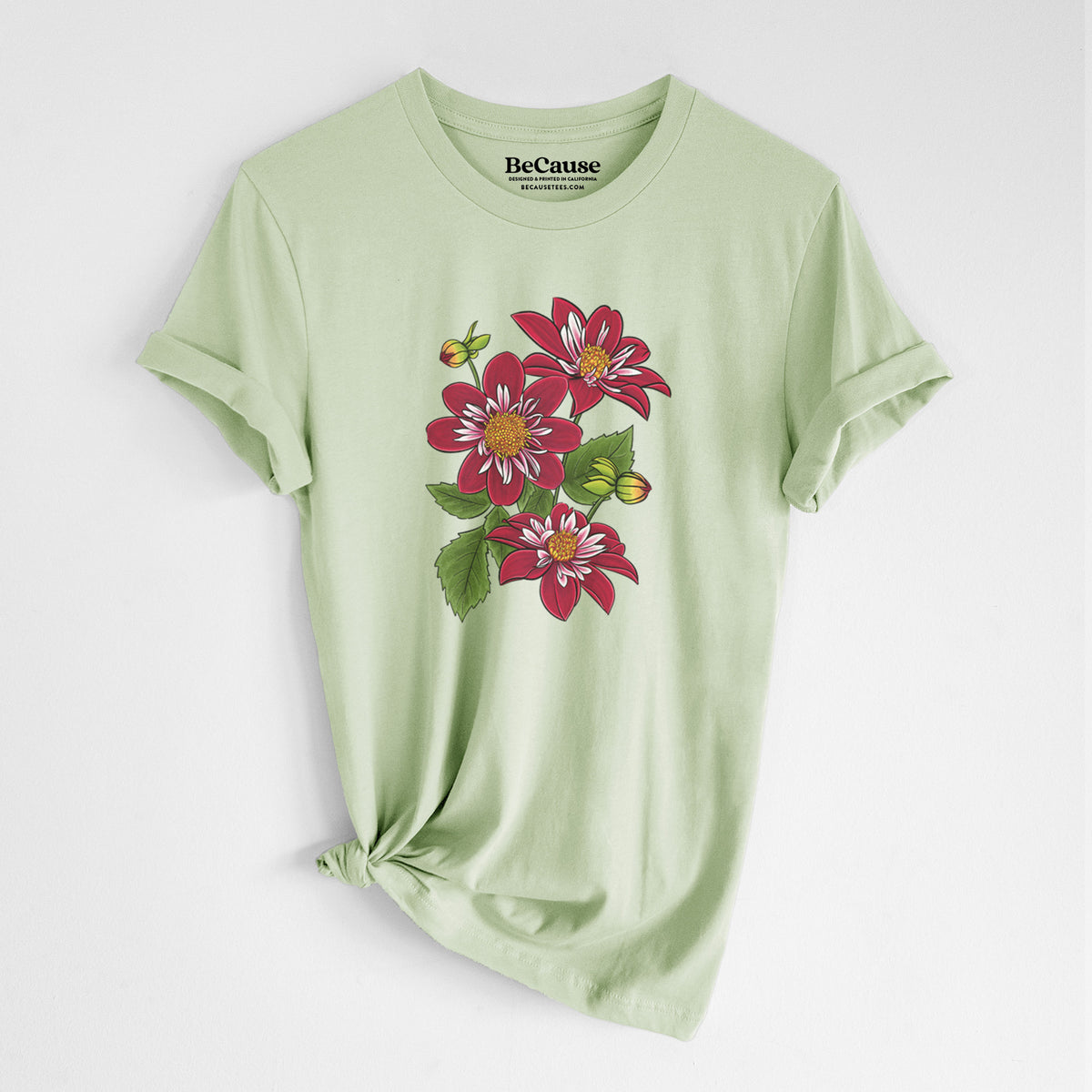 Spring green lightweight cotton t-shirt laid flat with the sleeves rolled, printed with a full-color illustration of deep red dahlia flowers with green leaves and a small bee.