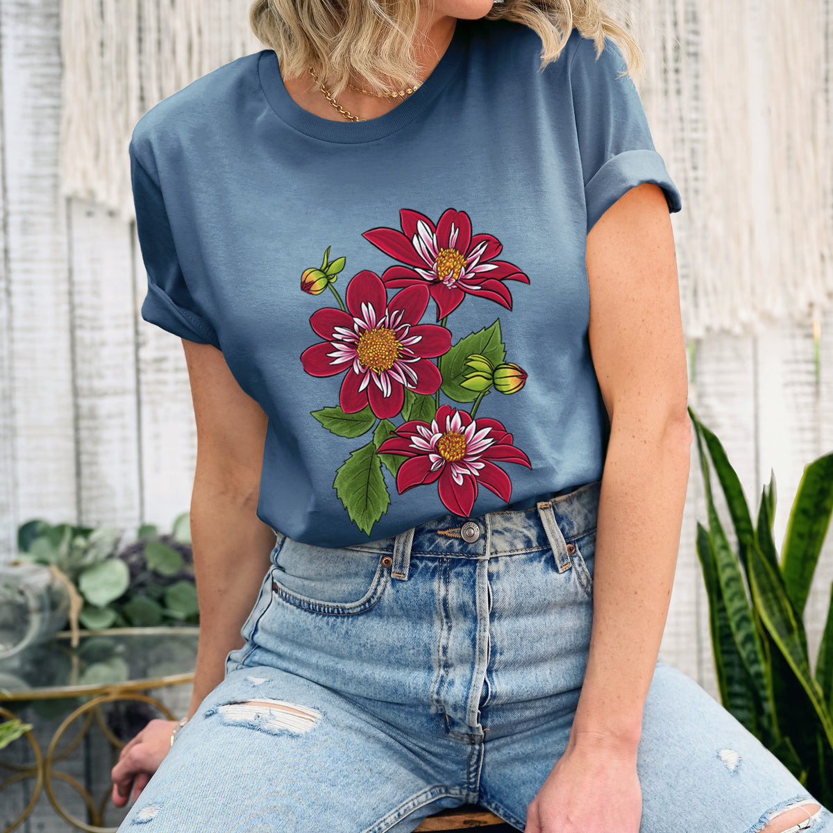 Woman wearing a steel blue lightweight cotton t-shirt printed with a full-color illustration of deep red dahlia flowers with green leaves and a small bee.