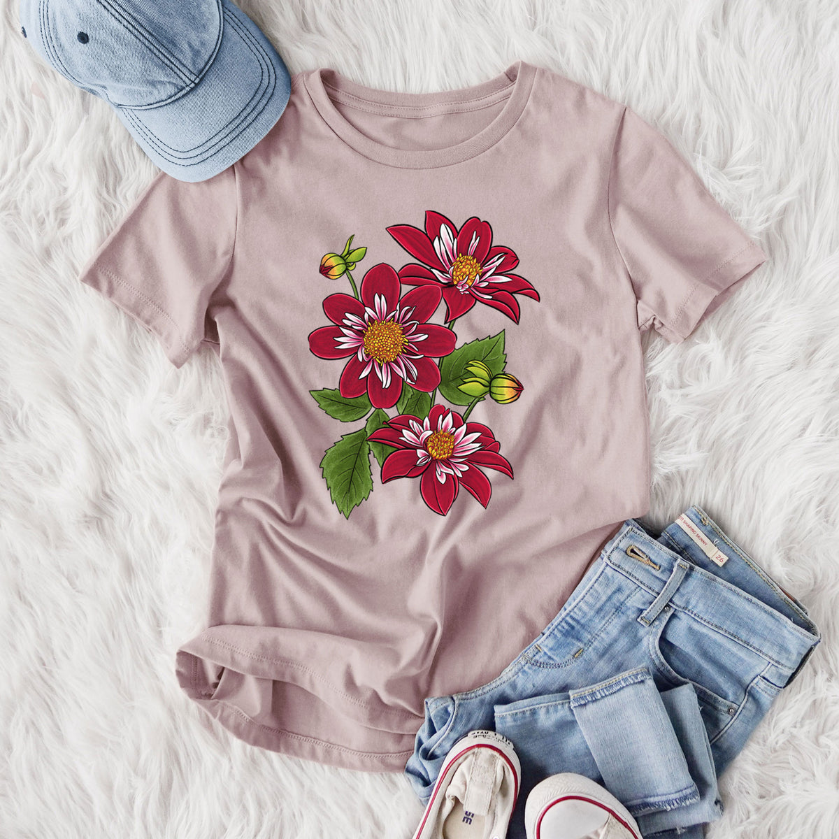 Women's relaxed fit cotton t-shirt printed with a full-color illustration of deep red dahlia flowers with green leaves and a small bee, styled flat on a white faux fur rug with jeans.