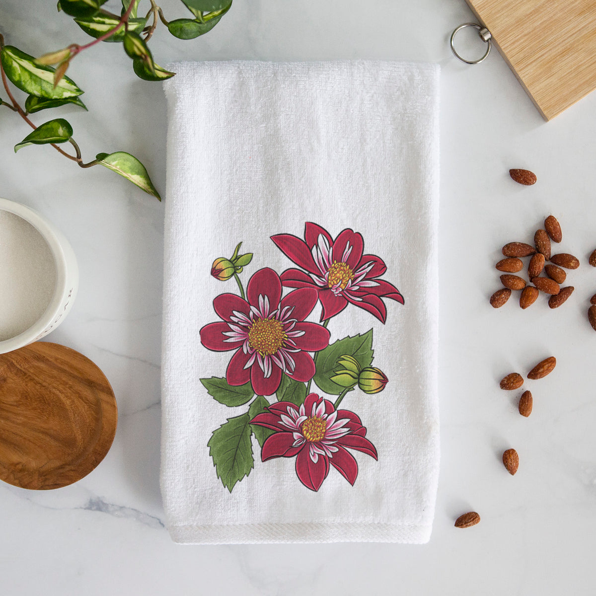 White hand towel printed with a full-color illustration of deep red dahlia flowers with green leaves and a small bee.