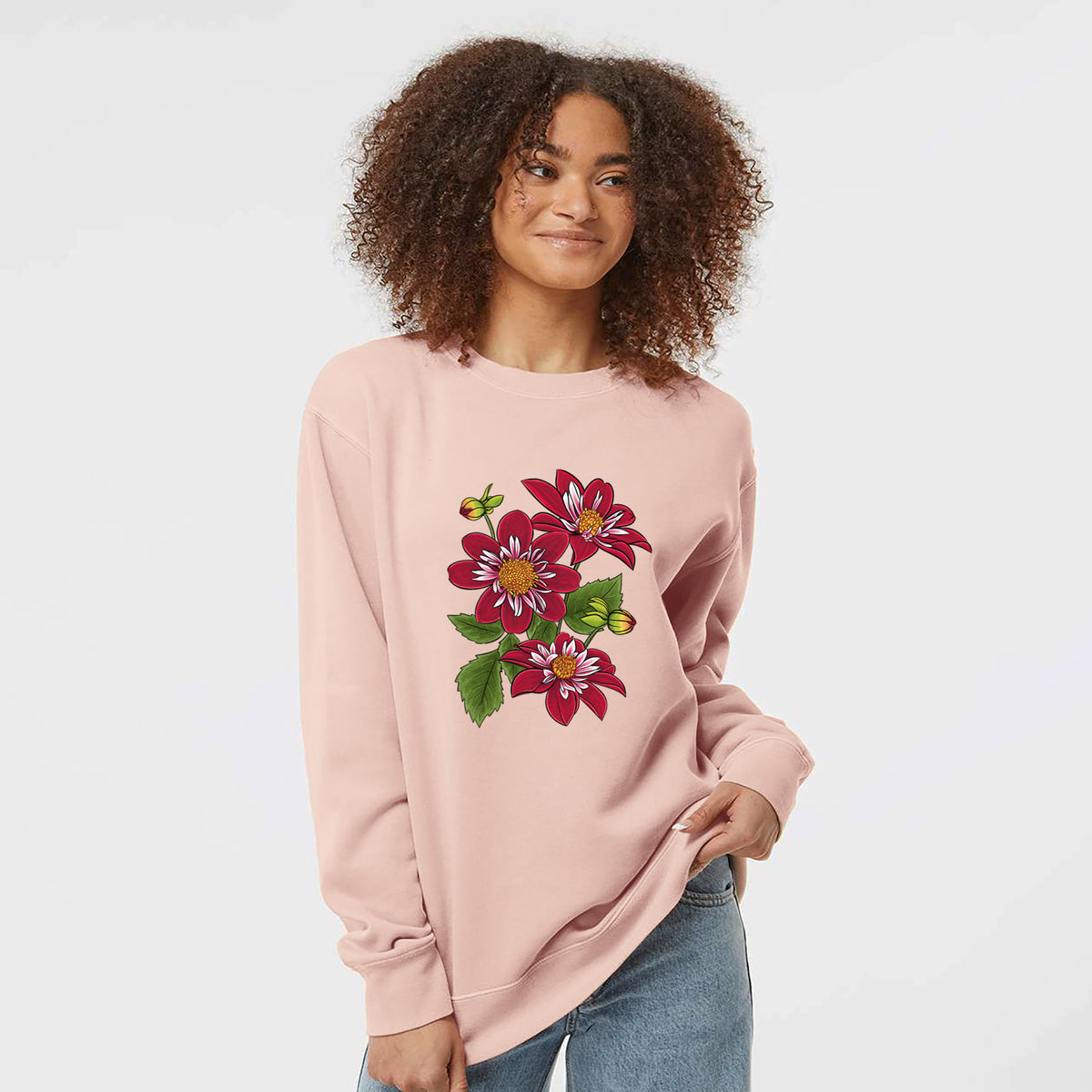 Model wearing a dusty pink pigment dyed crewneck sweatshirt printed with a full-color illustration of deep red dahlia flowers with green leaves and a small bee.