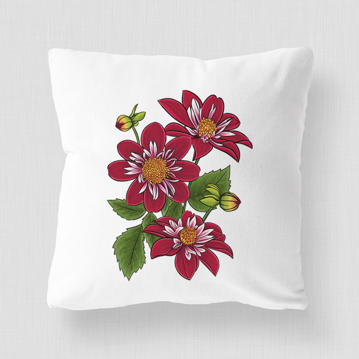 White pillow cover printed with a full-color illustration of deep red dahlia flowers with green leaves and a small bee.