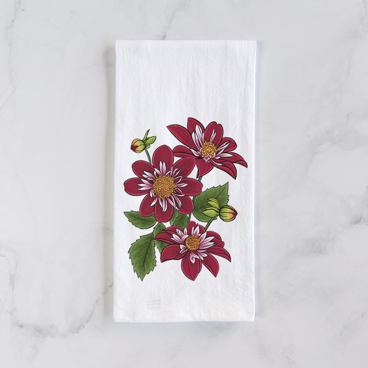 White cotton tea towel laid flat on marble, printed with a full-color illustration of deep red dahlia flowers with green leaves and a small bee.