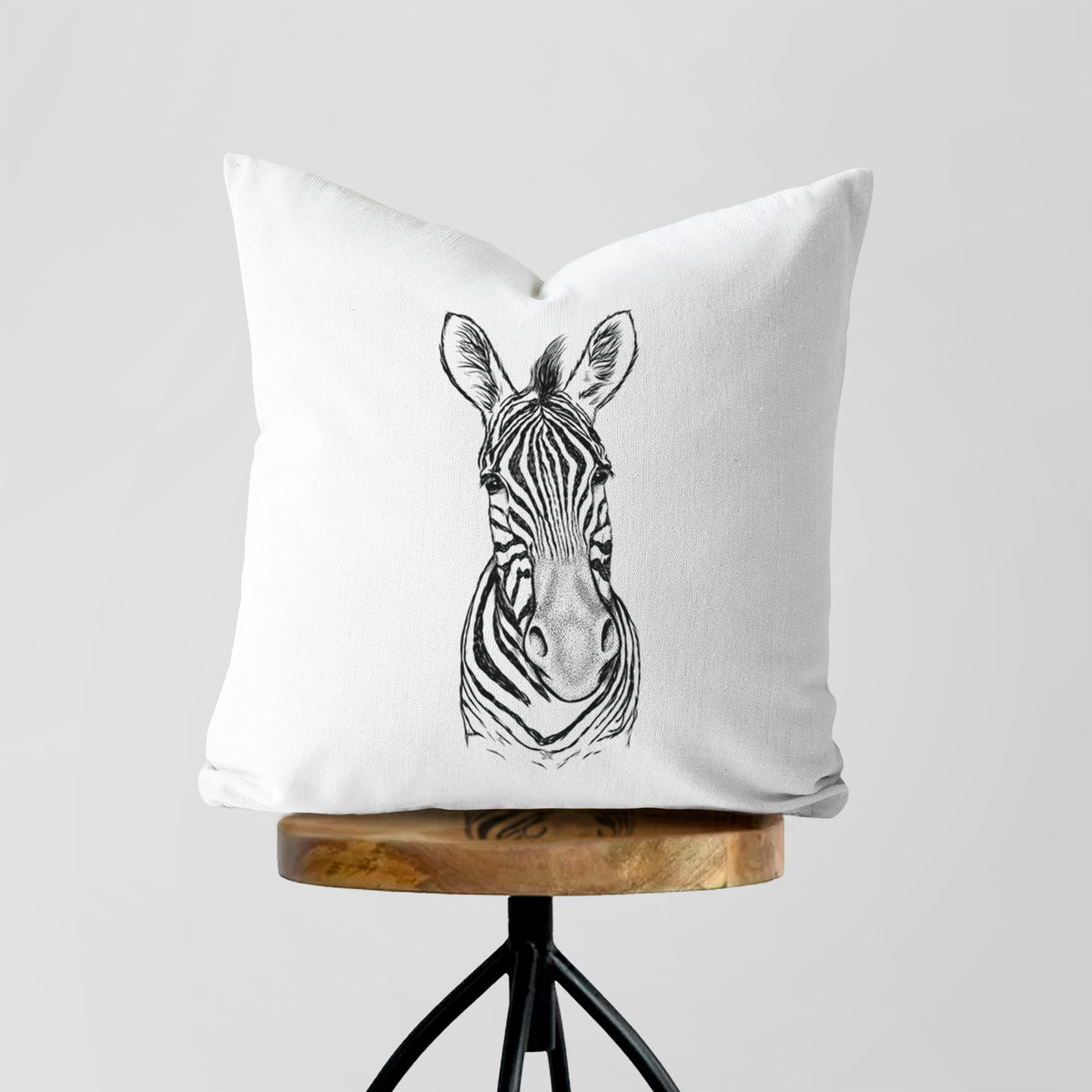 White pillow cover printed with a detailed black ink portrait of a Damara zebra facing forward, on a wooden stool.