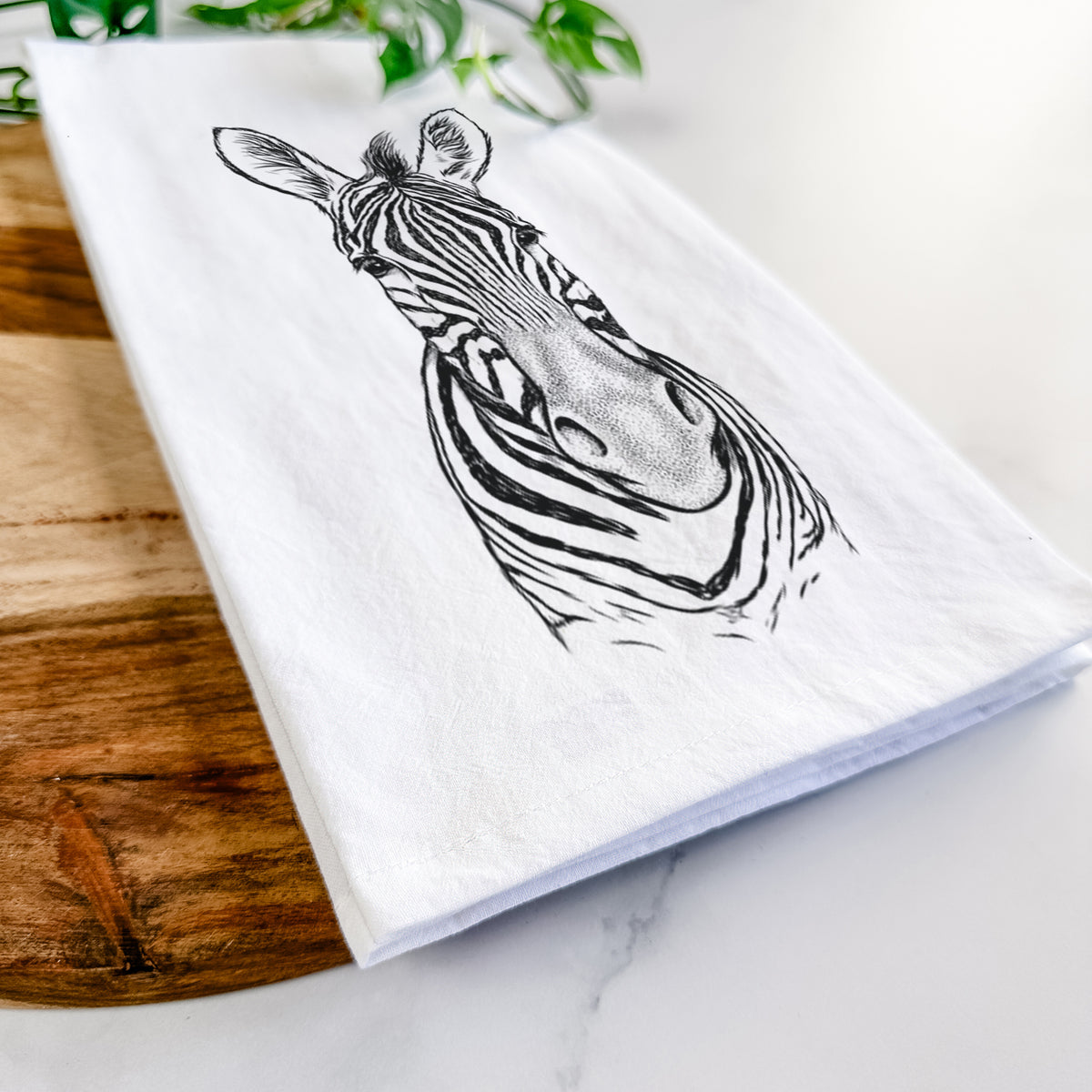 Close-up of a folded white tea towel on a wooden board, showing a detailed black ink portrait of a Damara zebra facing forward.