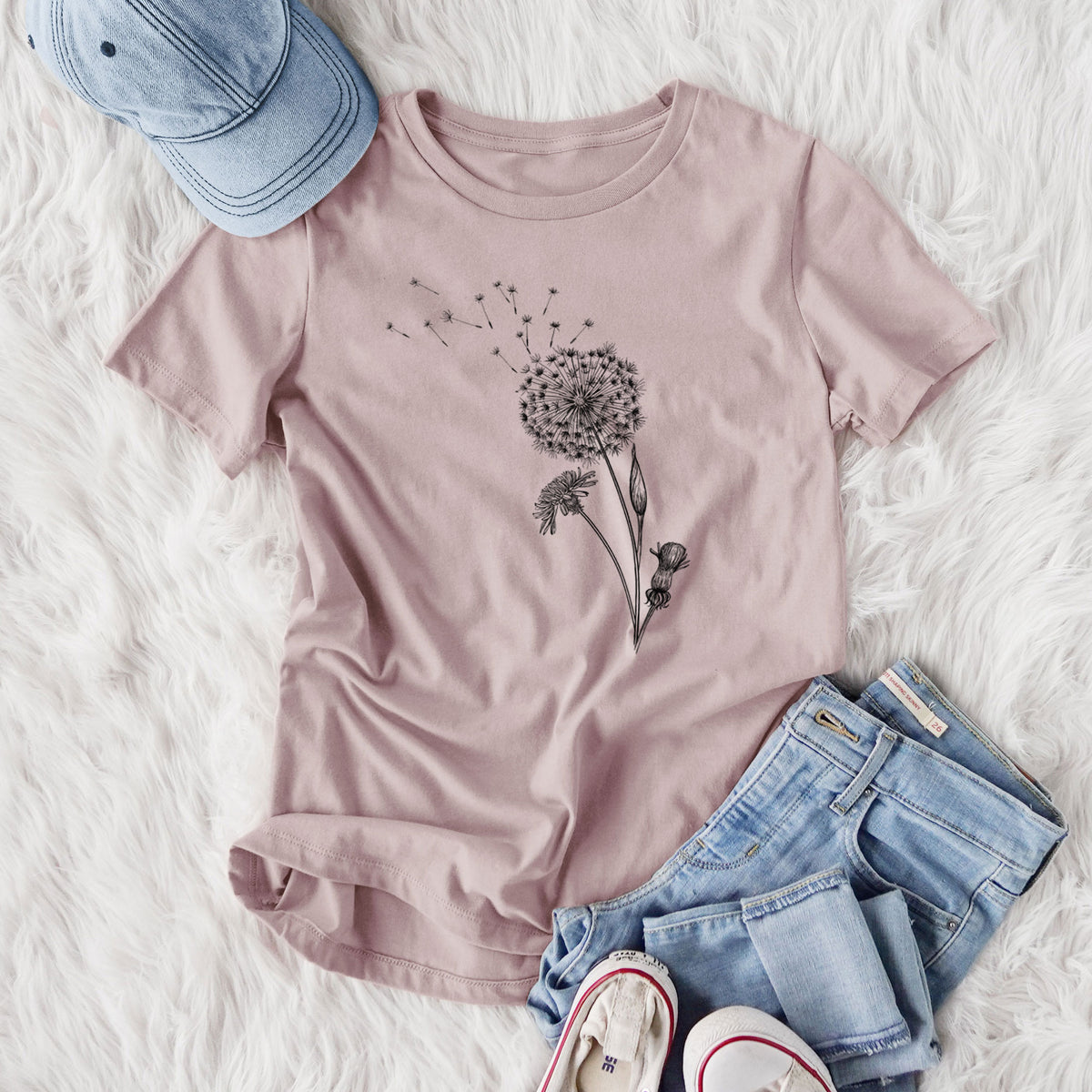 Women's relaxed fit cotton t-shirt printed with a black ink line drawing of a dandelion seed head with seeds blowing away, styled flat on a white faux fur rug with jeans.