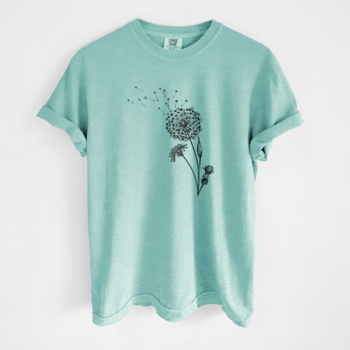 Chalky mint Comfort Colors t-shirt laid flat, printed with a black ink line drawing of a dandelion seed head with seeds blowing away.