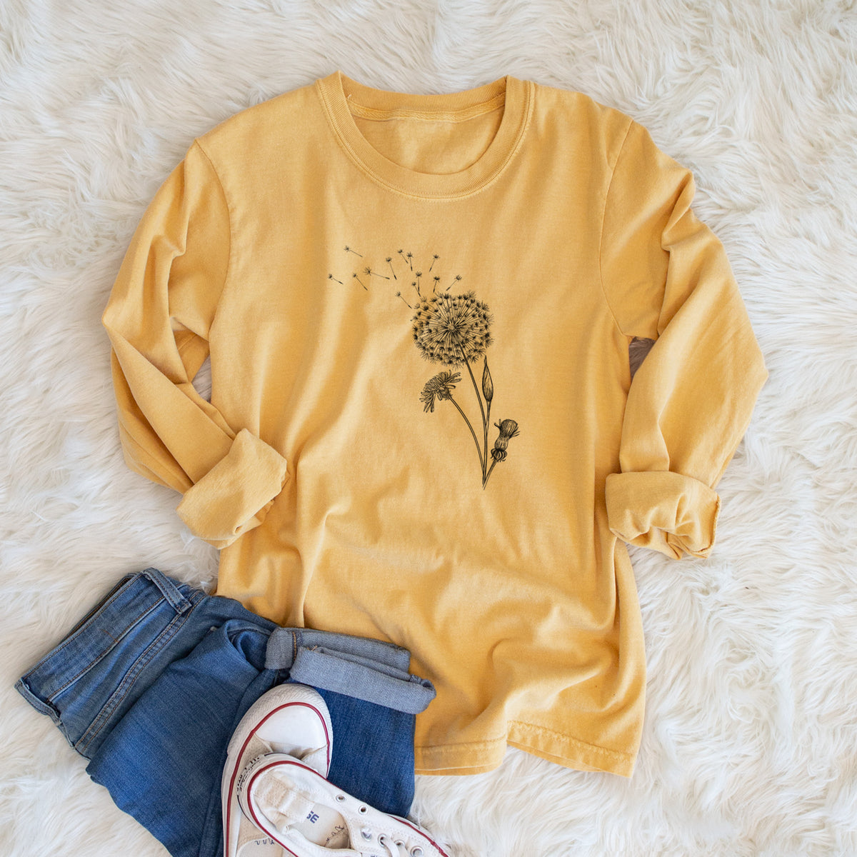 Golden wheat yellow Comfort Colors long sleeve shirt printed with a black ink line drawing of a dandelion seed head with seeds blowing away, shown in a lifestyle photo.