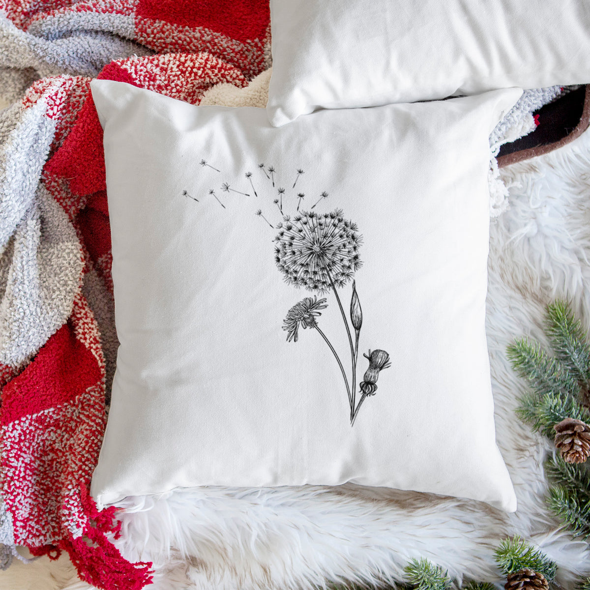 White pillow cover printed with a black ink line drawing of a dandelion seed head with seeds blowing away, on a woven chair.