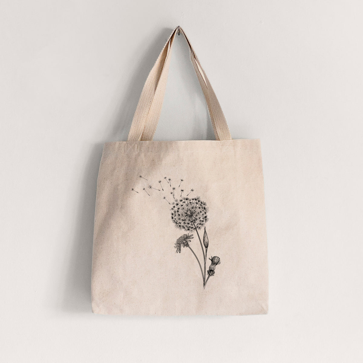 Natural canvas tote bag printed with a black ink line drawing of a dandelion seed head with seeds blowing away.