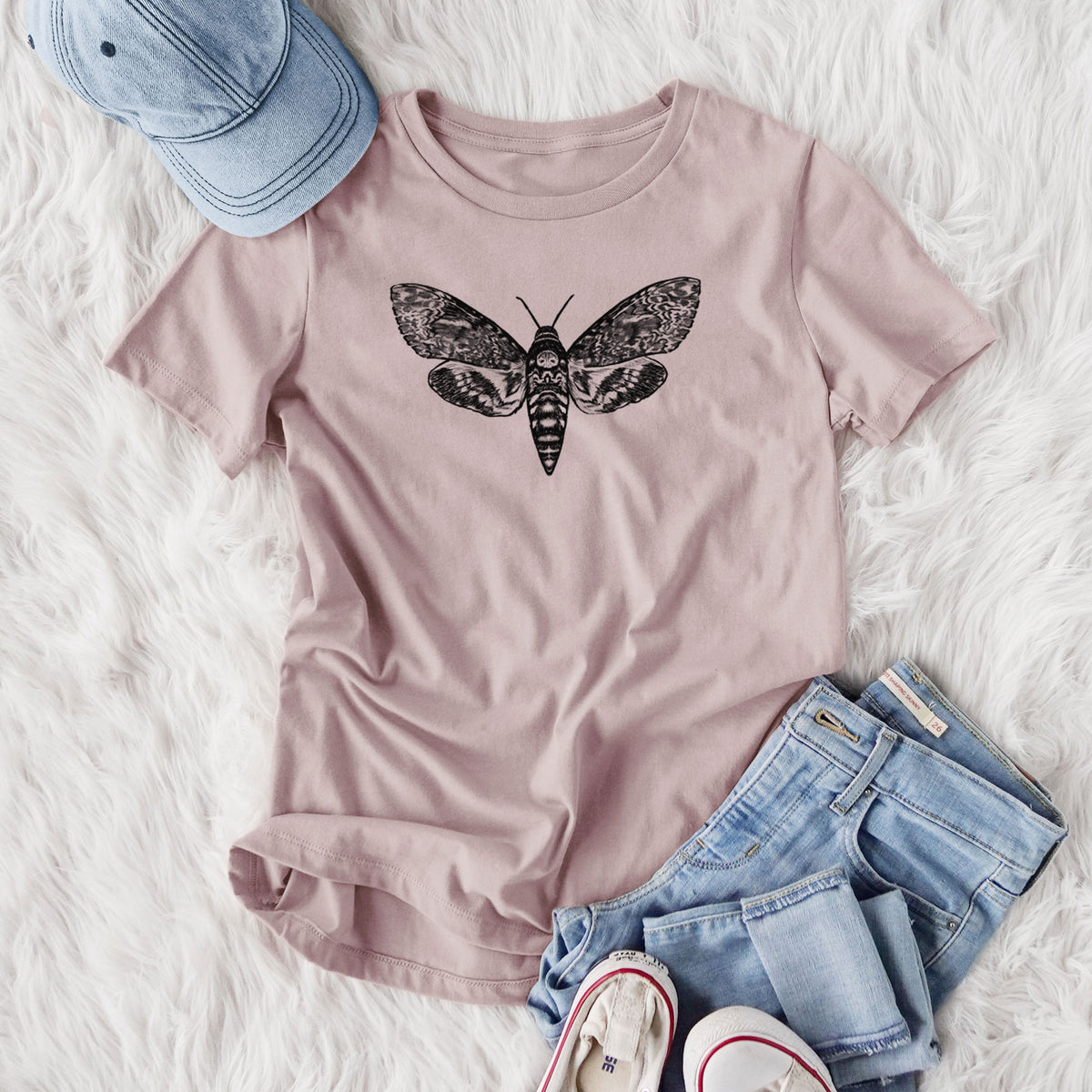 Women's relaxed fit cotton t-shirt printed with a detailed black ink illustration of a death's-head hawkmoth with its wings spread, styled flat on a white faux fur rug with jeans.