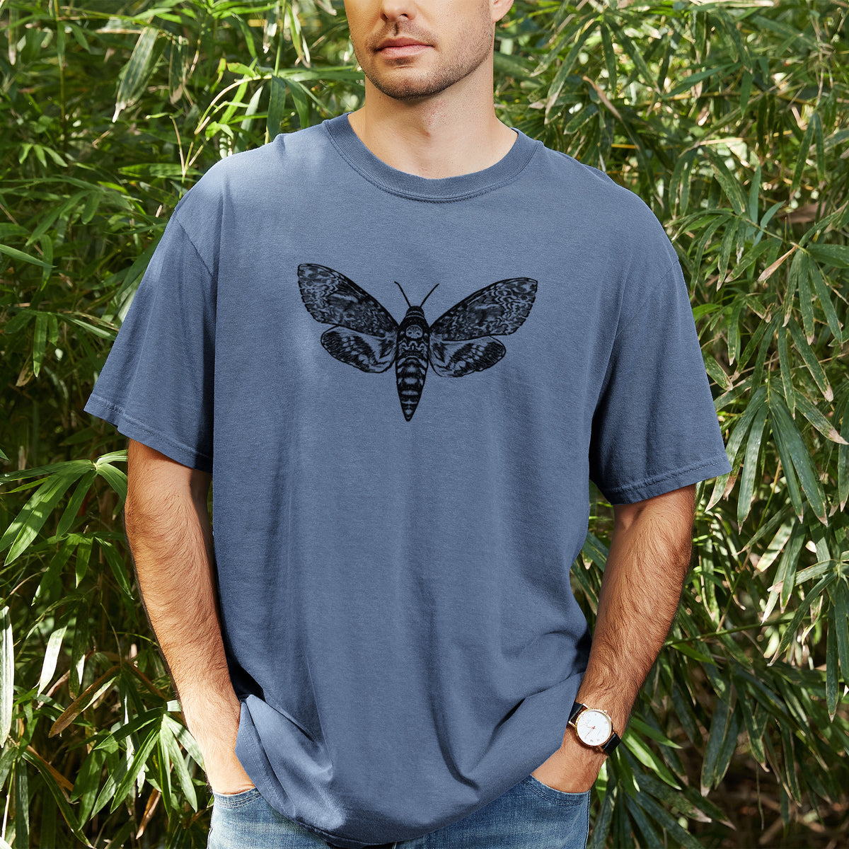 Man wearing a Comfort Colors t-shirt printed with a detailed black ink illustration of a death's-head hawkmoth with its wings spread, outdoors.