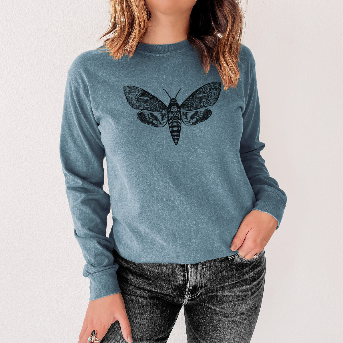 Steel blue Comfort Colors long sleeve shirt printed with a detailed black ink illustration of a death's-head hawkmoth with its wings spread, shown in a lifestyle photo.