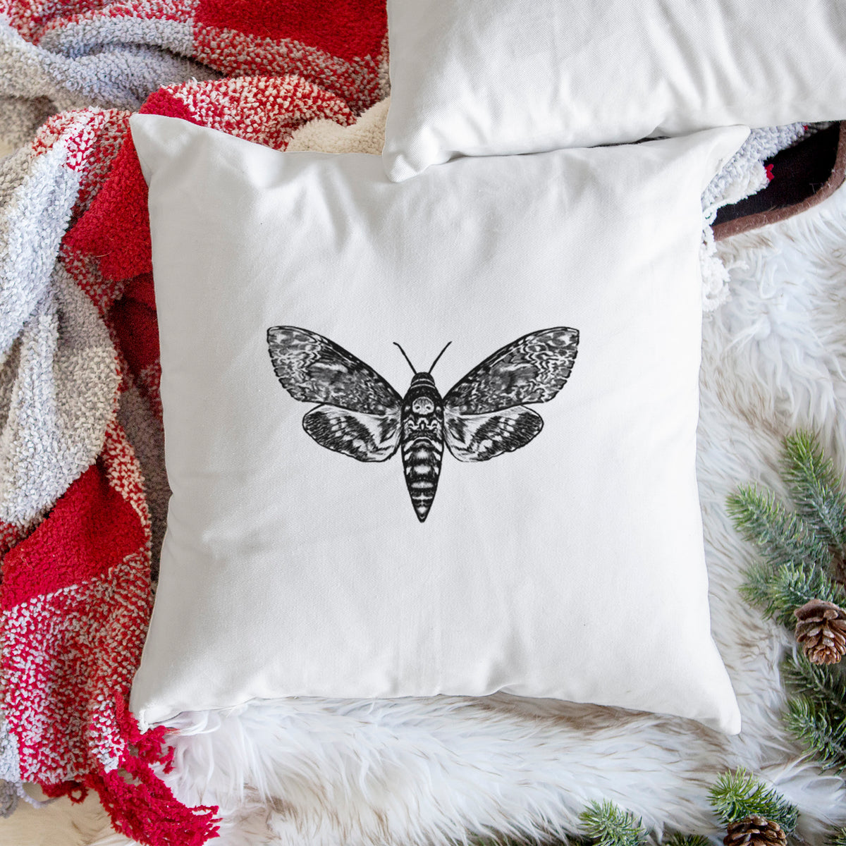 White pillow cover printed with a detailed black ink illustration of a death's-head hawkmoth with its wings spread, on a woven chair.