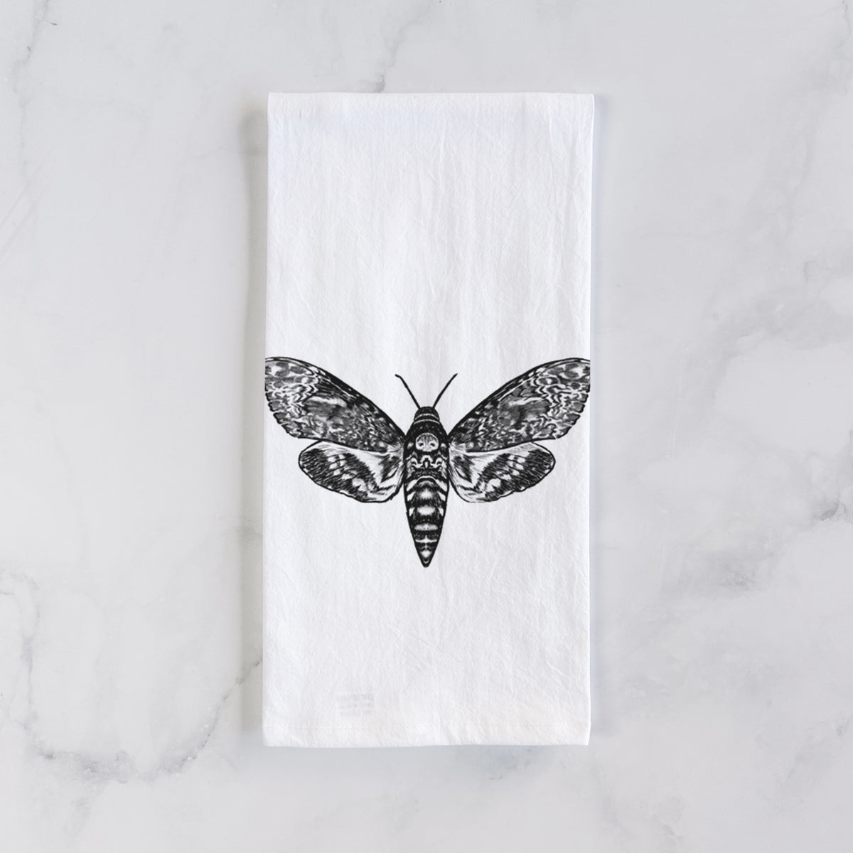 White cotton tea towel laid flat on marble, printed with a detailed black ink illustration of a death's-head hawkmoth with its wings spread.