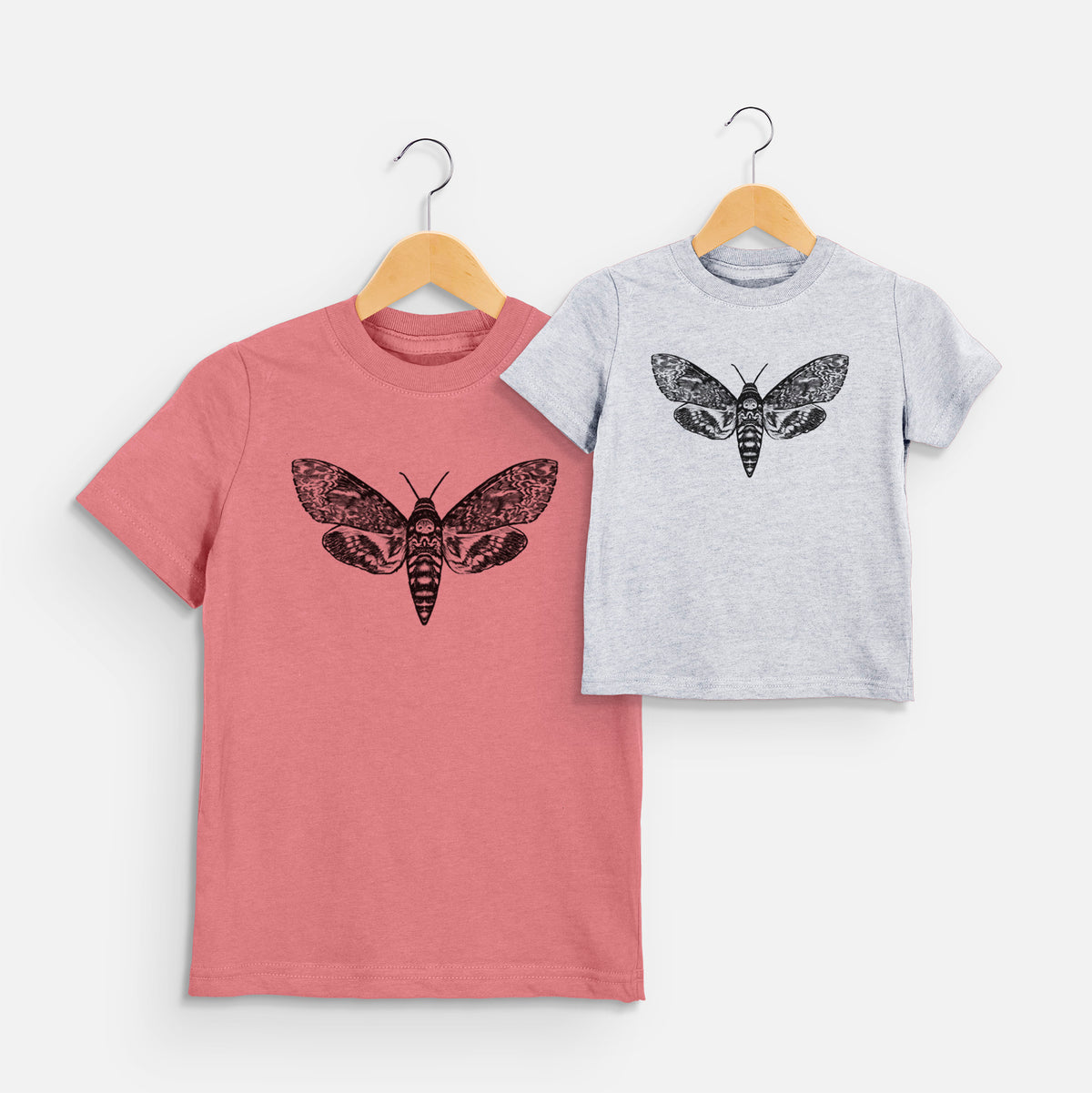 Two youth t-shirts in different colors on hangers, printed with a detailed black ink illustration of a death's-head hawkmoth with its wings spread.