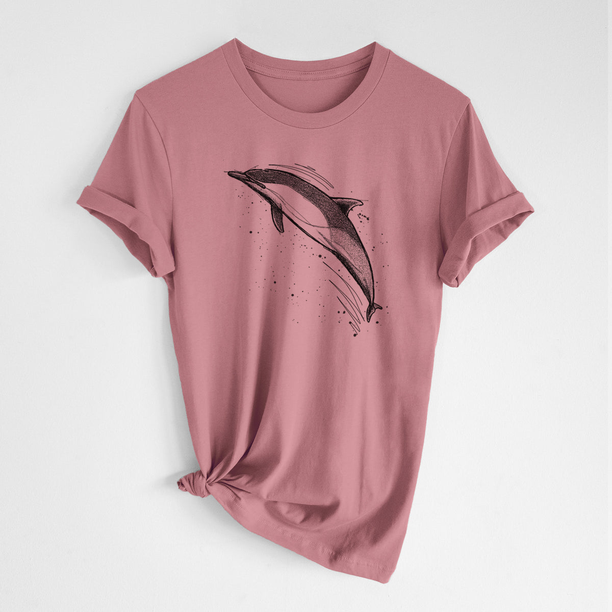 Mauve pink lightweight cotton t-shirt laid flat with the sleeves rolled, printed with a black ink illustration of a common dolphin leaping, with ink splatters.