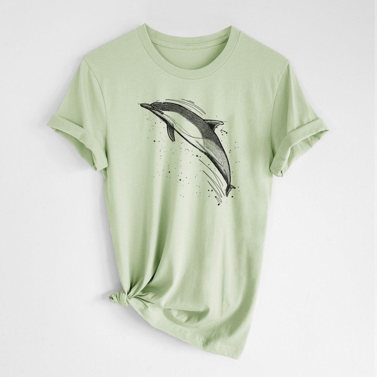 Spring green lightweight cotton t-shirt laid flat with the sleeves rolled, printed with a black ink illustration of a common dolphin leaping, with ink splatters.