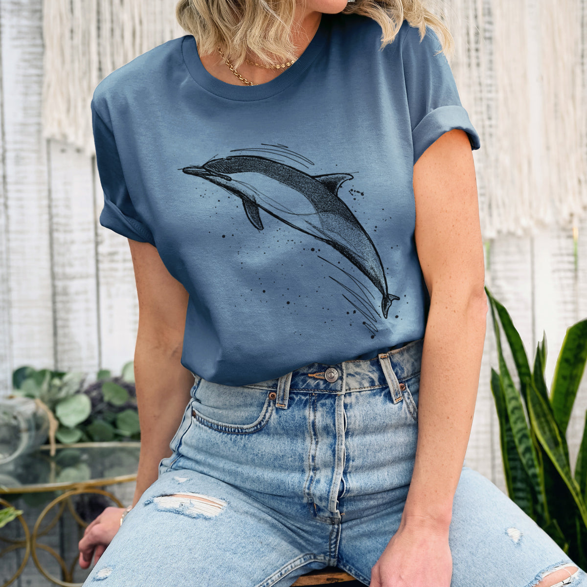Woman wearing a steel blue lightweight cotton t-shirt printed with a black ink illustration of a common dolphin leaping, with ink splatters.