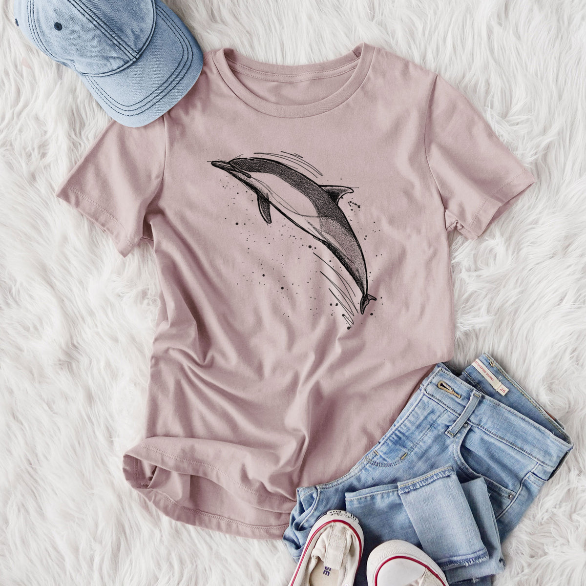 Women's relaxed fit cotton t-shirt printed with a black ink illustration of a common dolphin leaping, with ink splatters, styled flat on a white faux fur rug with jeans.