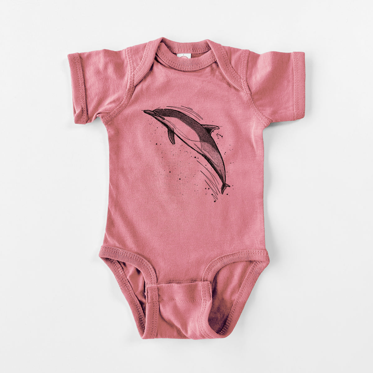 Mauve pink baby bodysuit laid flat, printed with a black ink illustration of a common dolphin leaping, with ink splatters.