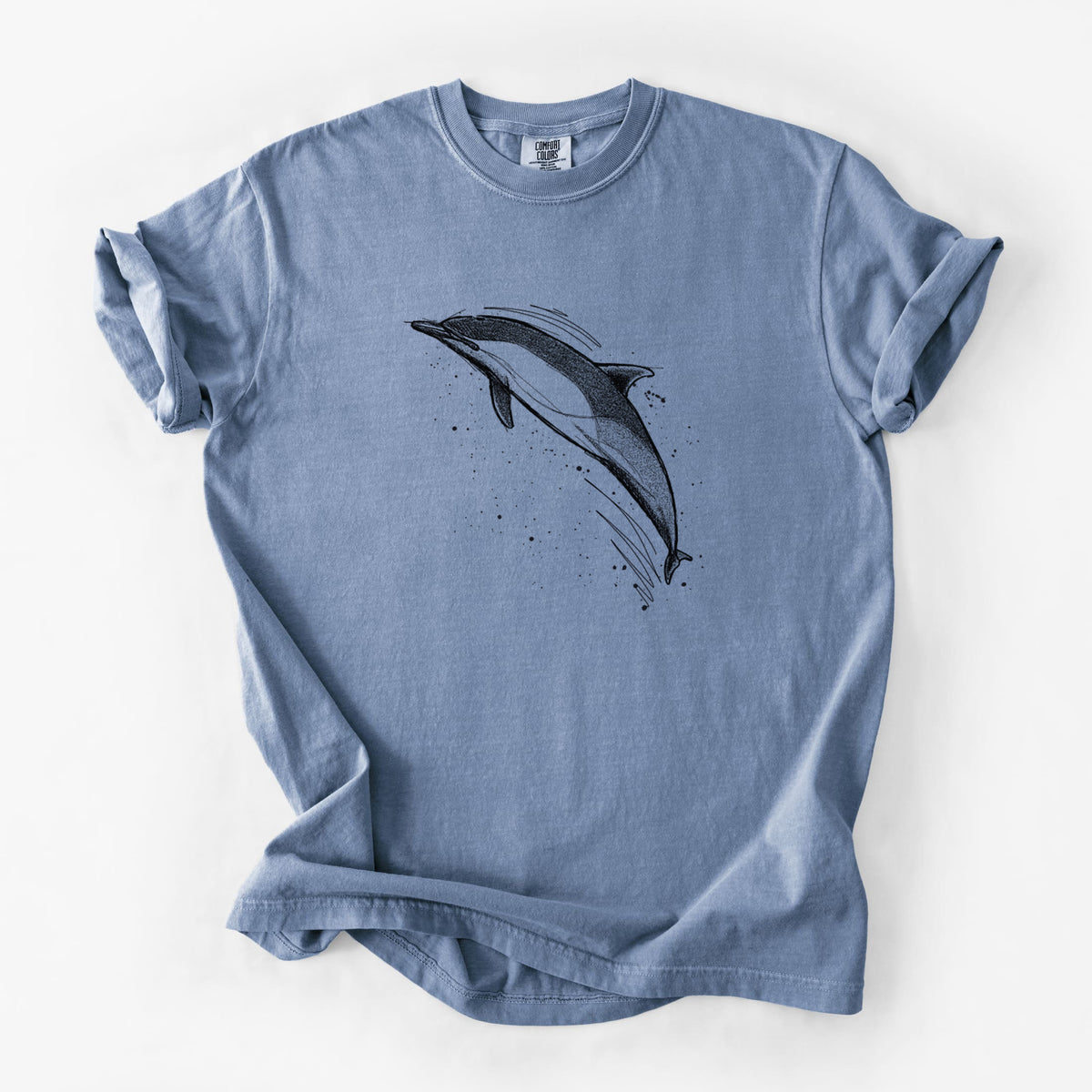 Blue jean Comfort Colors t-shirt laid flat, printed with a black ink illustration of a common dolphin leaping, with ink splatters.