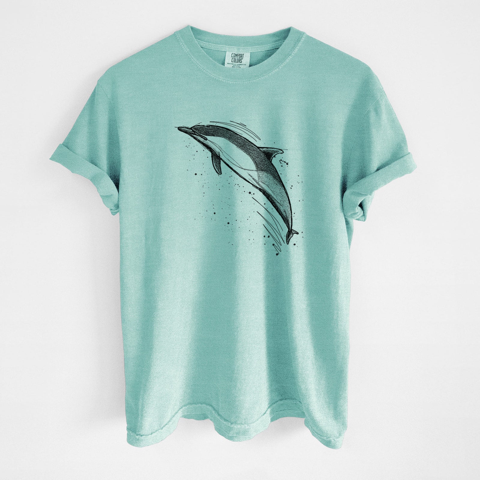 Blue jean Comfort Colors t-shirt laid flat, printed with a black ink illustration of a common dolphin leaping, with ink splatters.