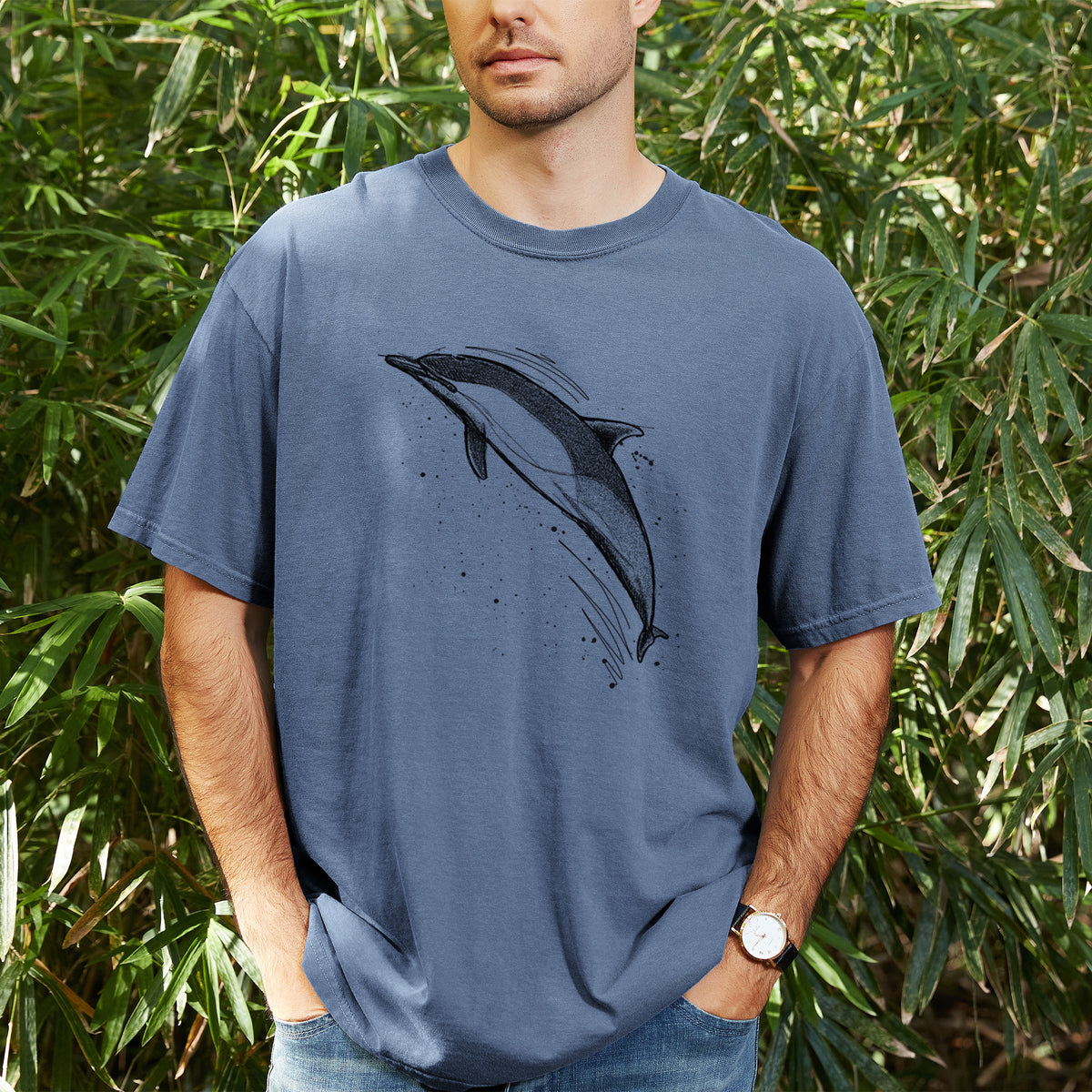 Man wearing a Comfort Colors t-shirt printed with a black ink illustration of a common dolphin leaping, with ink splatters, outdoors.