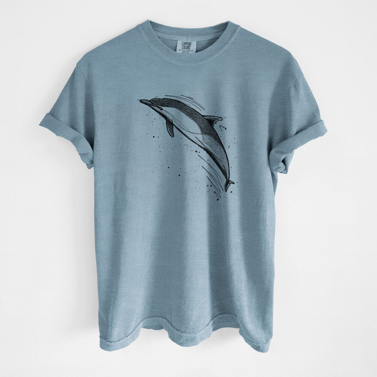 Steel blue Comfort Colors t-shirt laid flat, printed with a black ink illustration of a common dolphin leaping, with ink splatters.