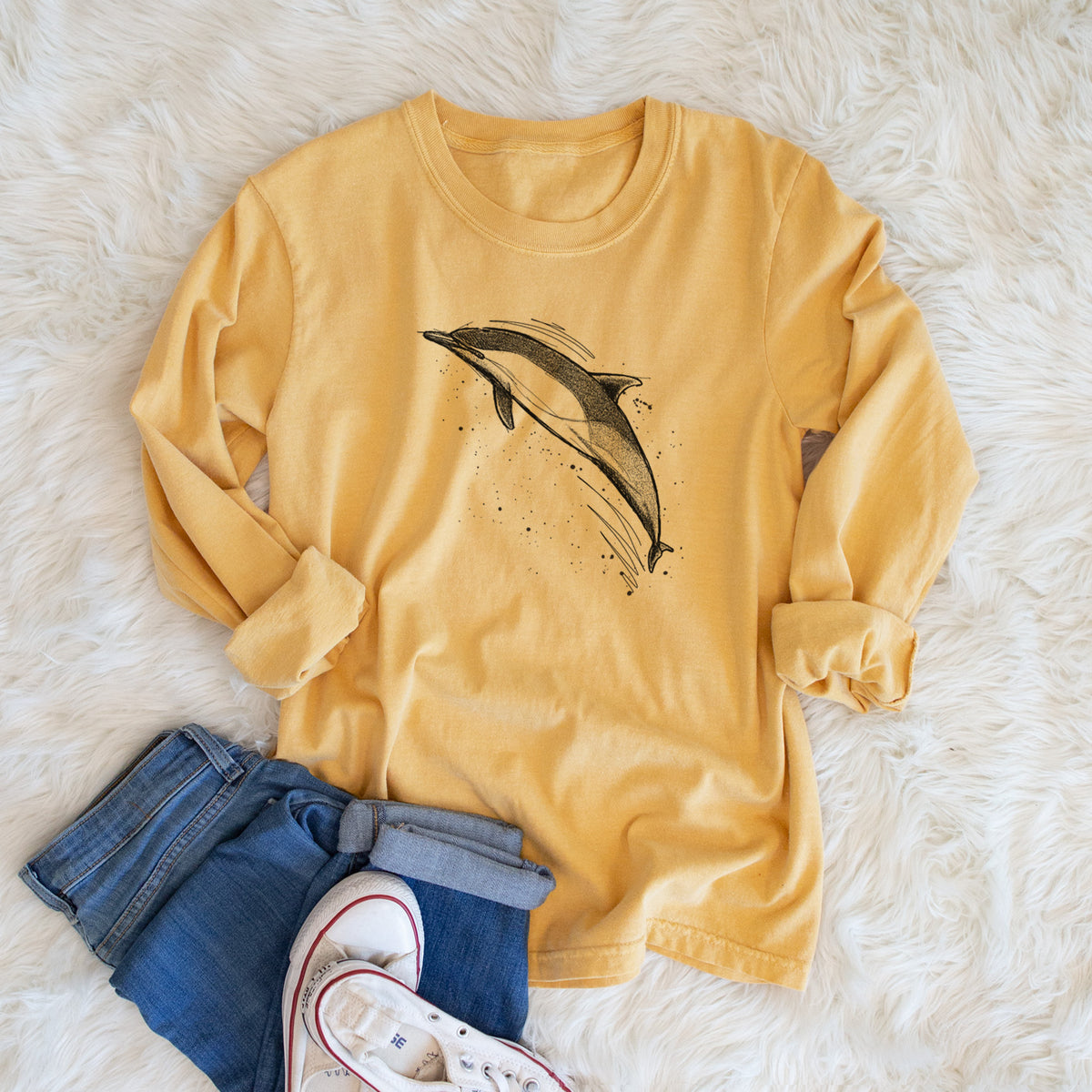 Golden wheat yellow Comfort Colors long sleeve shirt printed with a black ink illustration of a common dolphin leaping, with ink splatters, shown in a lifestyle photo.