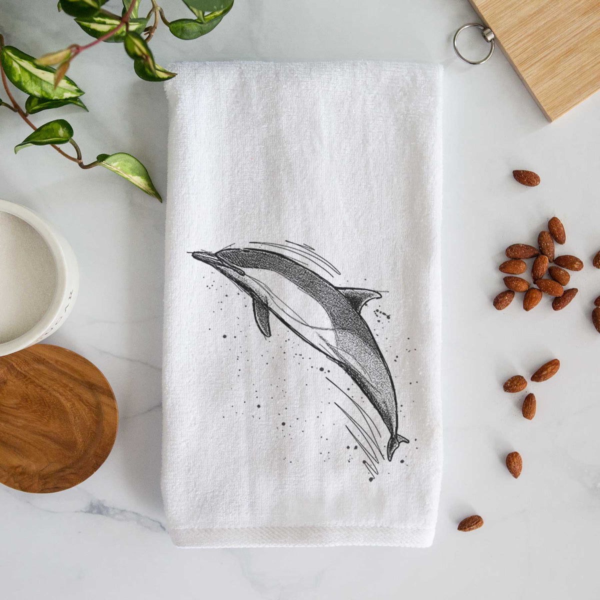White hand towel printed with a black ink illustration of a common dolphin leaping, with ink splatters.