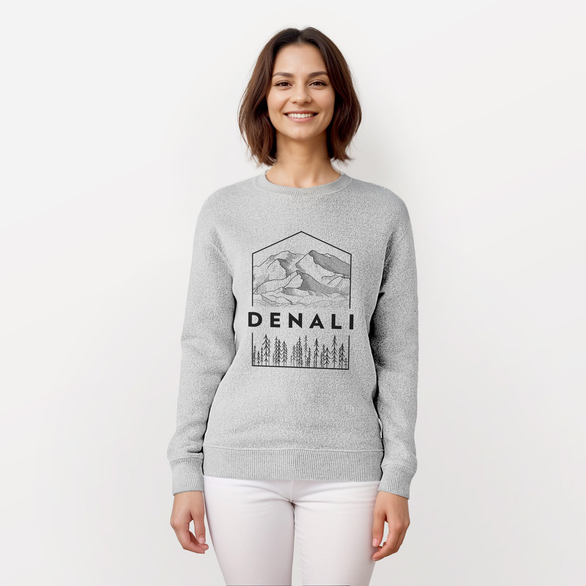 Woman wearing a knit sweatshirt printed with a black line art badge of the Denali mountain range above pine trees, with the word Denali.