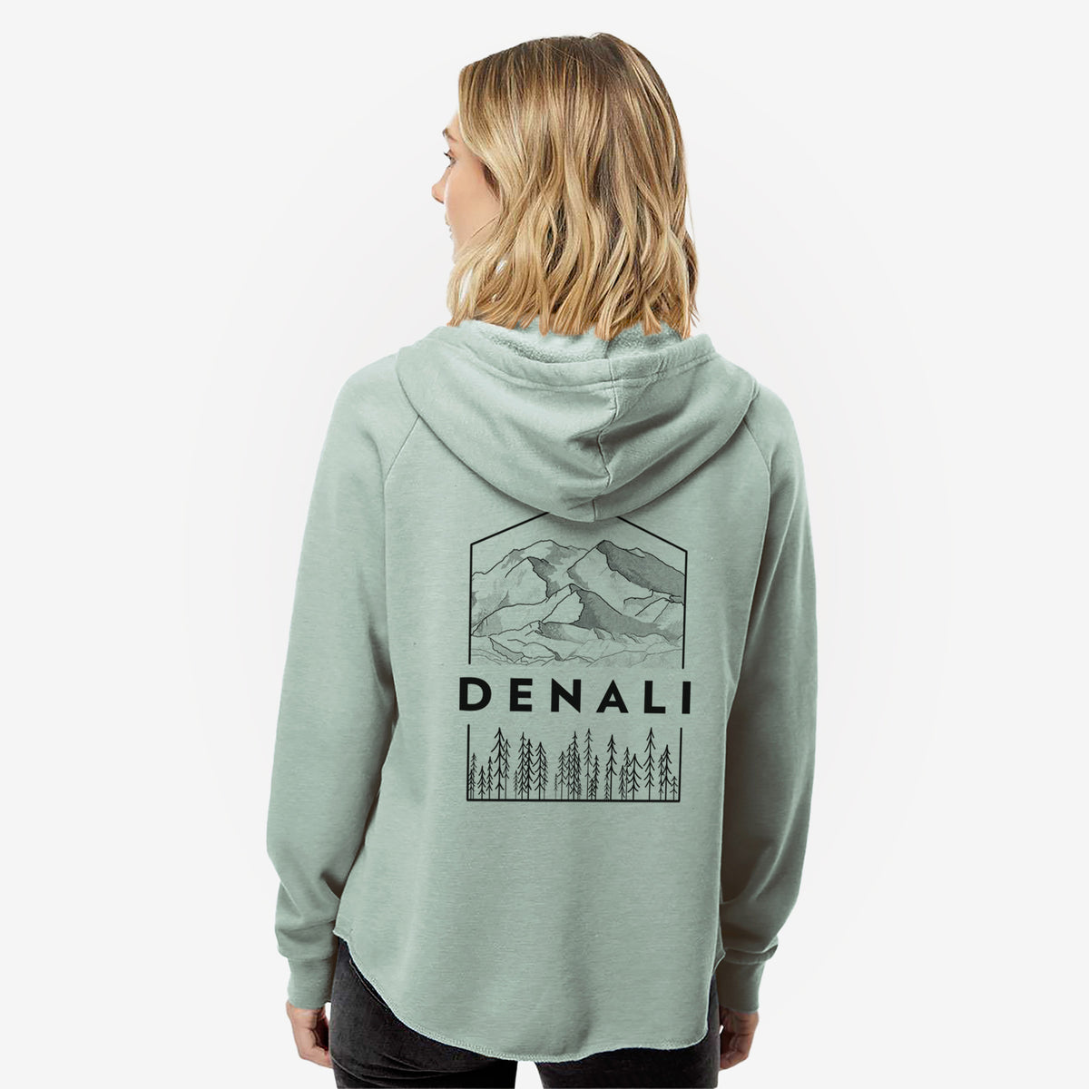 Woman wearing a sage green women's Cali Wave zip-up sweatshirt printed with a black line art badge of the Denali mountain range above pine trees, with the word Denali, seen from behind.