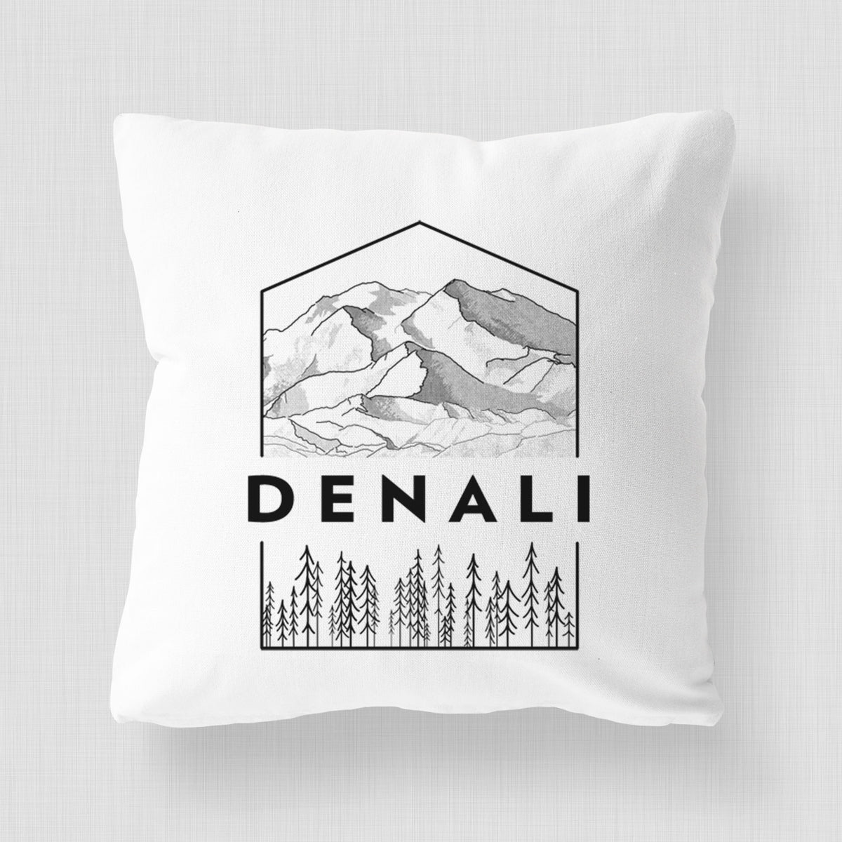 White pillow cover printed with a black line art badge of the Denali mountain range above pine trees, with the word Denali.
