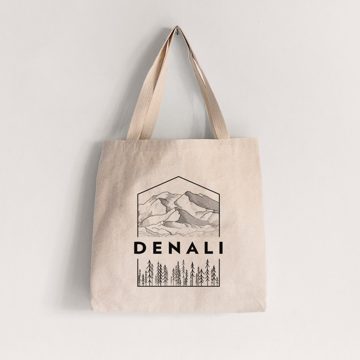 Natural canvas tote bag printed with a black line art badge of the Denali mountain range above pine trees, with the word Denali.