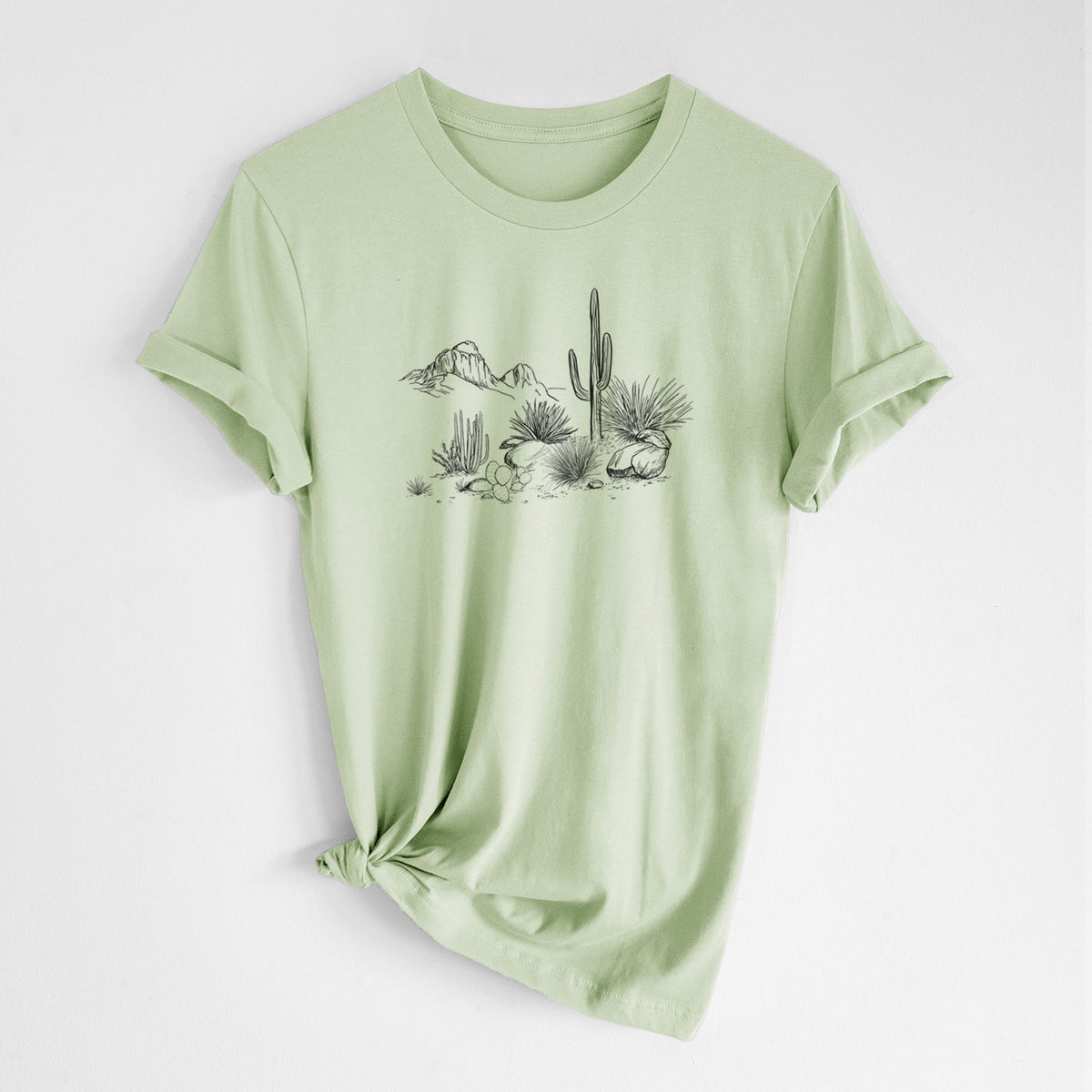 Spring green lightweight cotton t-shirt laid flat with the sleeves rolled, printed with a black ink desert scene with a saguaro cactus, agave, rocks and distant mountains.