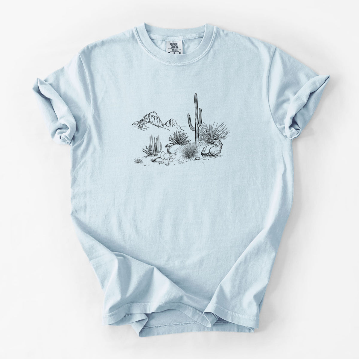 Chambray blue Comfort Colors t-shirt laid flat, printed with a black ink desert scene with a saguaro cactus, agave, rocks and distant mountains.