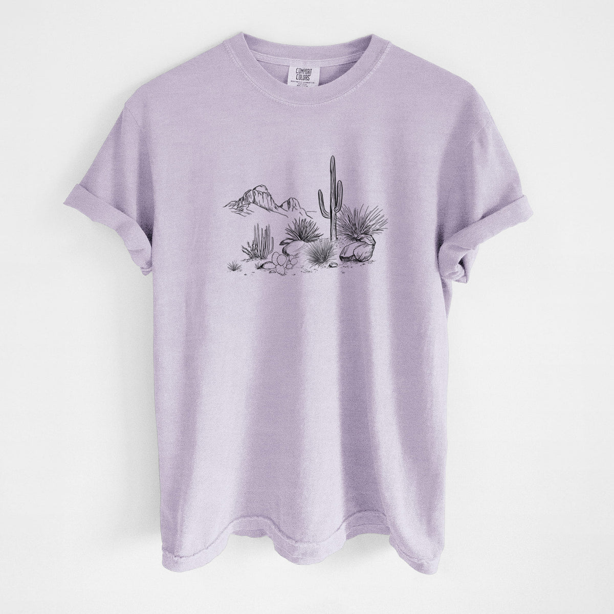 Orchid purple Comfort Colors t-shirt laid flat, printed with a black ink desert scene with a saguaro cactus, agave, rocks and distant mountains.