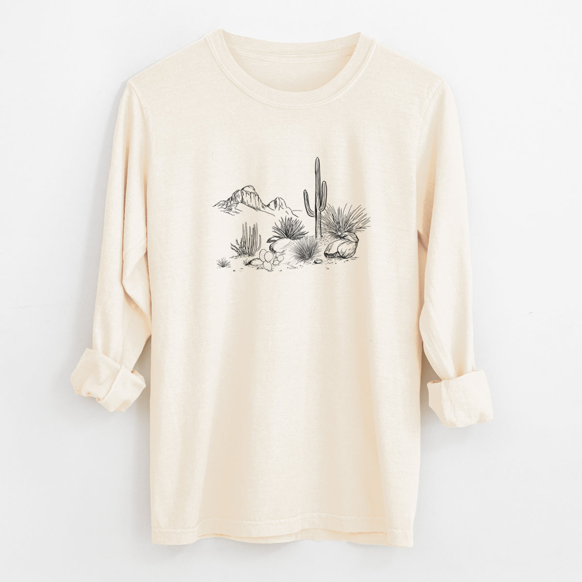Ivory Comfort Colors long sleeve shirt laid flat with the cuffs rolled, printed with a black ink desert scene with a saguaro cactus, agave, rocks and distant mountains.